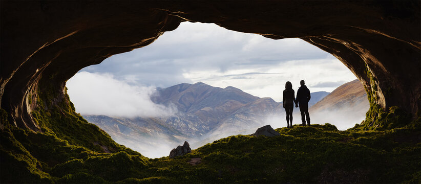 Adventurous Man and Woman Couple standing in a rocky cave. Mountain Nature Landscape with clouds in background. Sunny Sunrise or Sunset. 3d Rendering Adventure Art.