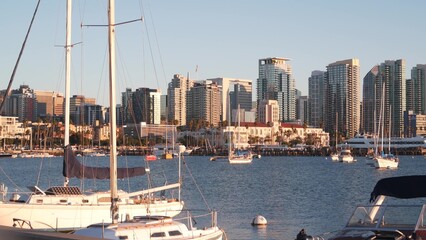 Fototapeta na wymiar Yachts in marina and downtown city skyline at sunset, San Diego cityscape, California coast, USA. Highrise skyscrapers, boat in bay, waterfront promenade. Urban architecture and sailboat in harbor.