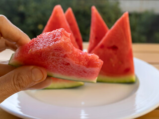 Close-up of ripe red seedless watermelon slice in hand  