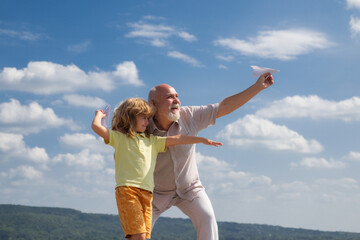 Grandfather and son playing with paper plane over blue sky and clouds background.