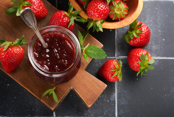 Strawberry jam. Strawberry jam in glass jar with fresh berries plate on an old black cracked tile table background, closeup. Homemade strawberry fruity jam. Top view with copy space.