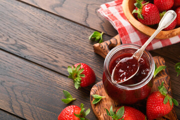Strawberry jam. Strawberry jam in glass jar with fresh berries plate on an old wooden dark table background, closeup. Homemade strawberry fruity jam. Top view with copy space.