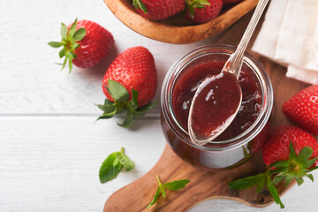 Strawberry jam. Strawberry jam in glass jar with fresh berries plate on white wooden table background, closeup. Homemade strawberry fruity jam. Top view with copy space.