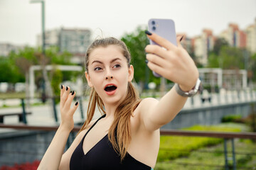 Happy sportive woman wearing sports bra standing on city park, outdoors having surprised face...