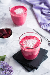 Delicious beetroot latte in glasses and beetroot pieces in a bowl on the table. Vertical view