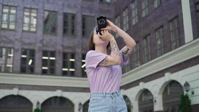 Young Girl Photographer Takes Pictures of City Architecture. Tattooed Girl with Camera Takes Pictures in City Center 