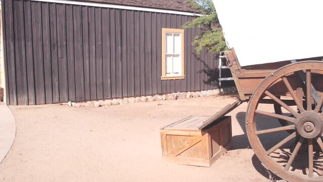 Old wooden retro covered wagon on wheels, wild west pioneer ranch. Western historic retro cart, traditional vintage transport. Rural house wall, building exterior. Countryside farm or cowboy saloon.