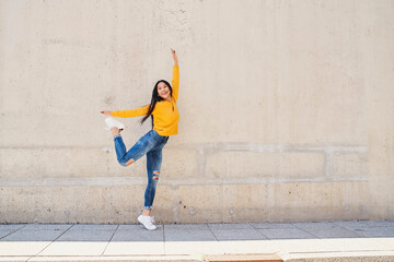 Joyful young asian woman dancing against concrete wall in the city
