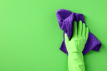 Female hand in green rubber glove with purple microfiber cloth wiping green wall. Cleaning service concept.