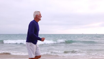A mature 66 year old man jogging at the beach in Southern California. Slow Motion.