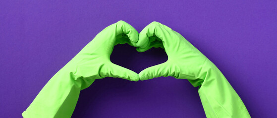 Heart shaped hands in green rubber gloves over purple background. House cleaning service and housekeeping concept.