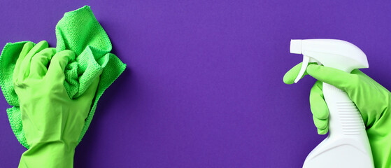Hand in rubber glove with microfiber green cloth and hand with spray bottle on purple background. Cleaning service banner design.