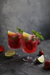 Refreshing strawberry lemonade with lemon basil, lime and ice. Two glasses with cold berry cocktail.