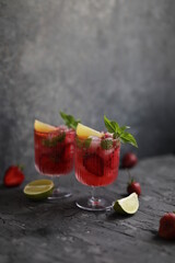 Refreshing strawberry lemonade with lemon basil, lime and ice. Two glasses with cold berry cocktail.