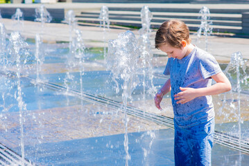 happy child plays in a dry fountain. joyful smiling boy stands wet in the fountain