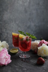 Refreshing strawberry lemonade with lemon basil, lime and ice. Two glasses with cold berry cocktail.
