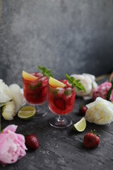 Refreshing strawberry lemonade with lemon basil, lime and ice. Two glasses with cold berry cocktail.