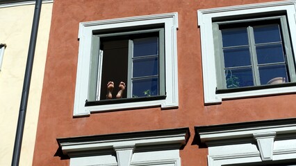 Two feet up emerge from a window in the historic center during a sunny morning.