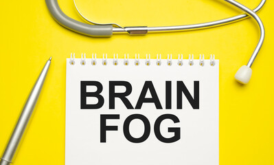 The word brain fog written on a white notepad on a yellow background