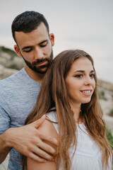 A close portrait of a Hispanic man who is stroking a Latina girlfriend on the rocky sea coast in Spain. A couple of tourists in the evening in a highland park in Valencia.