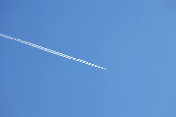 Smuga spalin zostaje za niebem za lecącym samolotem. - obrazy, fototapety, plakaty