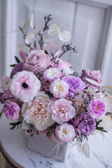 Light gray concrete planter with flowers. Gently pink anemones, pink roses and cream peonies with eucalyptus. Composition on a marble table. Floristics preserved flowers.