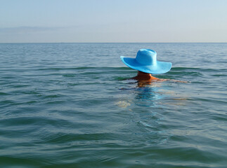 Fototapeta na wymiar Young woman girl in blue hat swimming in the sea ocean. Sunny weather clear sky reflections.