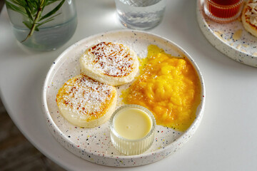 White plate with fried curd pancakes or syrniki, horizontal shot, sprinkled with coconut.