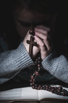Prayer to God. Close up portrait of young girl pray with rosary and reading the Bible. Vertical image.