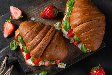 Croissant sandwiches with fresh strawberries, cream cheese and basil on black background. Top view