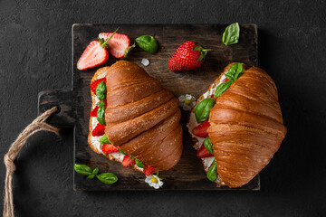 Delicious croissant sandwiches with fresh strawberry, soft cheese and basil on wooden cutting...