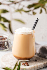 Cappuccino or latte with milk foam in a glass with coffee beans on light  marble background with branches close up. Front view