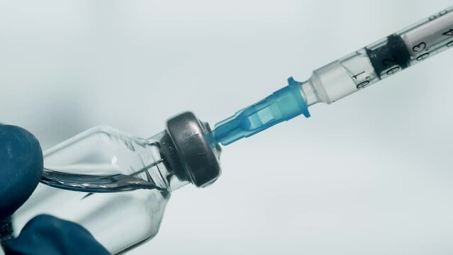 A doctor is drawing up vaccine from phial bottle and filling syringe injection for vaccination. Concept of health care treatment disease prevention and immunization. Close up.