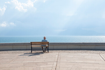 The old man sits on the bench and watches the sea..