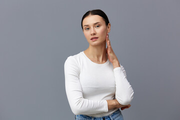 Obraz premium a cute woman with a ponytail on her head stands on a dark background in a white tight T-shirt, put her hand on her neck holding it with the other