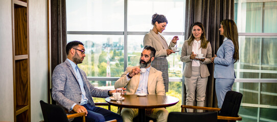 Coffee break at the office, two male colleagues talking and three young females drinking coffee