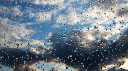 Raindrops on the glass. View of the sky with clouds after rain. Overcast clouds in the sky in the sun's rays, a view through wet glass.