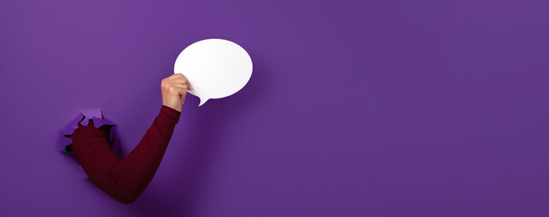 Talk bubble speech icon in hand over purple background, panoramic layout