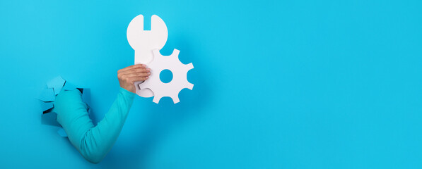 hand holding wrench and gear over blue background, concept of repair, panoramic layout