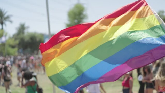 Slow motion of people waving the LGBTQ rainbow flag during a pride parade in a city streets
