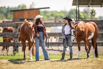 Two horse-riding girls discuss horses on a ranch while standing next to them