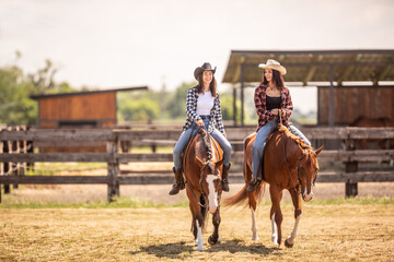 Two cowgirls riding their horses on a ranch during hot summer day