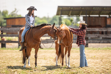 Two female friends on a ranch are getting ready for a horse ride