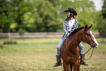 The paint horse and the girl riding it both look in opposite directions during a ride on the farm