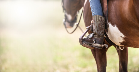 Detail of a ornamented cowboy boots in a stirrup while sitting on a horse - obrazy, fototapety, plakaty