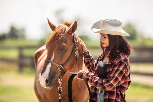 Beautiful girl in a hat and checkered shirt talks to calm a paint horse out in a ranch
