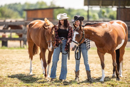Two female friends and two brown paint horses together on a farm
