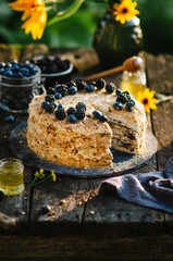 Homemade honey cake with prunes on a wooden table in nature. Cake decorated with blueberries and blackberries. Summer cake. Photo in rustic style.