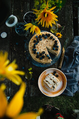 Homemade honey cake with prunes on a wooden table in nature. Cake decorated with blueberries and blackberries. Top view. Photo in rustic style.