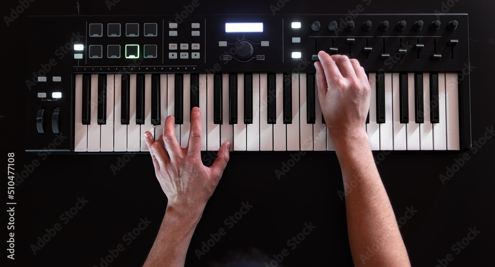 Wall mural a male hands play on white musical keys on a black background.